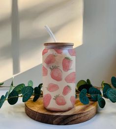 a glass with strawberries painted on it sitting next to some leaves and greenery