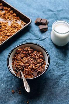 a bowl of granola next to a glass of milk and some chocolate bars on a table