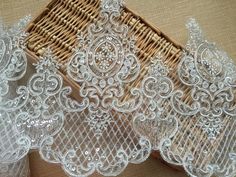 three pieces of white lace sitting on top of a wooden table next to a basket