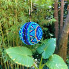 a blue ornament hanging from a tree with green leaves and trees in the background