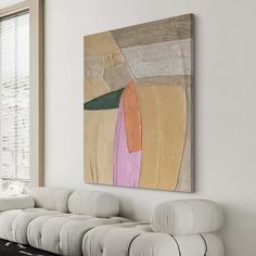 an abstract painting hangs on the wall above a white bench in front of a window