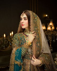 a woman in a green and gold bridal outfit with jewelry on her head, standing next to a chandelier