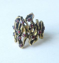 Modernistic free style with a darker gold tone. Depending how the light hits the ring the gemstones give off a red to light blue color. It is 10K gold with a ringsize of 5 1/2. See all photos. 0.\ Yellow Gold Multi-stone Ruby Ring, Yellow Gold Multi-stone Rings For Party, Unique Multi-stone Ruby Ring In Yellow Gold, Multi-stone Ruby Ring In Yellow Gold, Gold Ruby Gemstone Ring For Parties, Vintage Gold Jeweled Rings, Gold Ruby Ring With Multi-stone Detail, Unique Multi-stone Ruby Ring, Gold Ruby Ring With Multi-stone