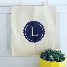 a tote bag with the letter l on it next to a potted plant