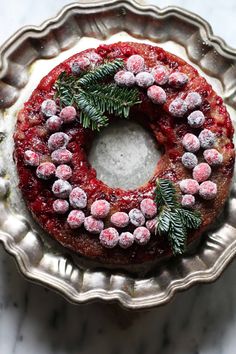 a cake covered in powdered sugar and sprinkled with christmas greenery sits on a silver platter