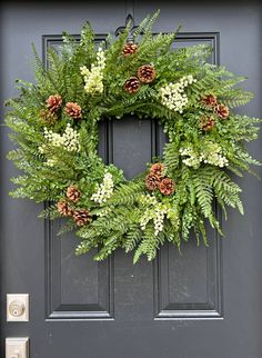 a green wreath with pine cones and white flowers