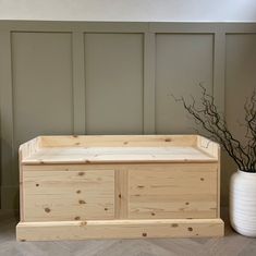 a white vase with some branches in it next to a wooden box on the floor