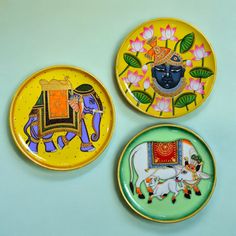 three colorful plates with designs on them sitting on a blue tableclothed surface, one has an elephant and the other is a bull