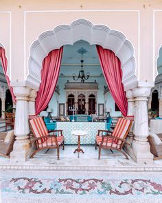 two chairs sitting in front of a table with red drapes on top of it