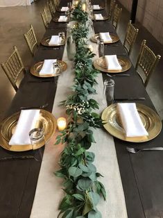 a long table set with gold plates and greenery on the runner, surrounded by candles