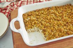 a casserole dish filled with food on top of a wooden cutting board next to a plate