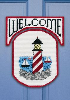 a welcome sign with a lighthouse and sailboats in the background on a blue door