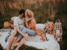 a man and woman sitting on a blanket in the grass