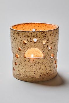 a ceramic candle holder with holes in the middle and a lit candle inside it on a white surface