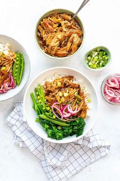 two bowls filled with meat and veggies on top of a white tablecloth