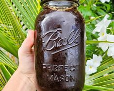 a person holding a mason jar in front of some flowers and palm tree leaves with the word ball on it