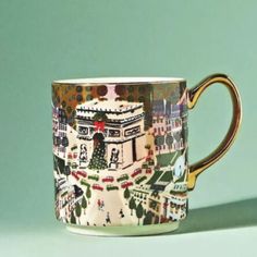 a coffee cup with a city scene painted on the side and gold rimmed handle