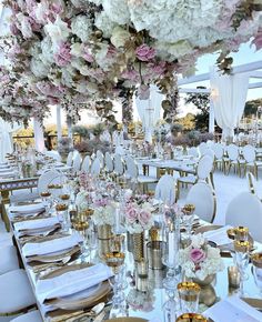 tables set up for an event with white and pink flowers hanging from the ceiling over them