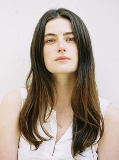 a woman with long hair is posing for a photo in front of a white wall