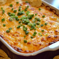 a casserole with green onions and cheese in a dish next to crackers