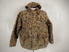 "Vintage 1940s hunting jacket, hooded coat. Made of brown camouflage cotton. Has a corduroy zippered split hood, chinstrap, four pockets, back game pouch, cotton flannel lined cowl and a button front. No label. Size large. Actual measurements are: 52\" at the chest 52\" at the waist 21\" shoulder seam to shoulder seam 22\" shoulder seam to end of cuff 26.5\" overall length In very good condition, nice natural fade." Military-style Brown Hunting Outerwear, Brown Military Style Hunting Outerwear, Camouflage Hooded Hunting Outerwear, Brown Military Style Outerwear For Hunting, Vintage Utility Jacket For Hunting In Fall, Vintage Hooded Hunting Outerwear, Vintage Long Sleeve Parka For Hunting, Vintage Hooded Outerwear For Hunting, Camouflage Utility Jacket For Fall Hunting