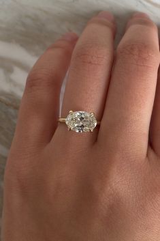 a woman's hand with a diamond ring on top of her left hand and the other hand holding an engagement ring