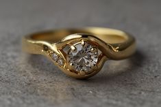 a yellow gold ring with a diamond in the center on a gray surface, close up