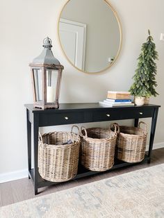 a black console table with three baskets underneath it and a round mirror on the wall