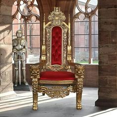 an ornate gold throne with red velvet seat in front of large arched windows and statues