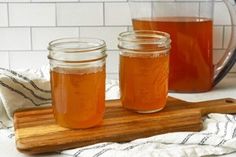 three jars filled with liquid sitting on top of a wooden cutting board next to a glass pitcher