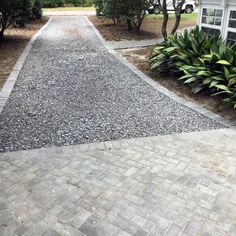 a gravel driveway with trees and bushes in the background