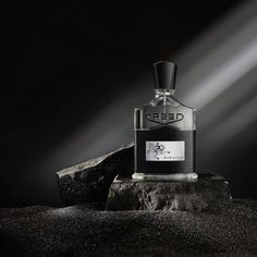 a bottle of perfume sitting on top of a rock next to a light shining from behind it