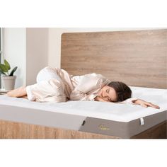 a woman laying on top of a mattress in a room with wooden headboard and white walls