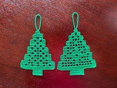 two crocheted christmas trees hanging from green string on a wooden table with red background