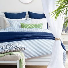 a bed with blue and white comforters in a bedroom next to a potted plant