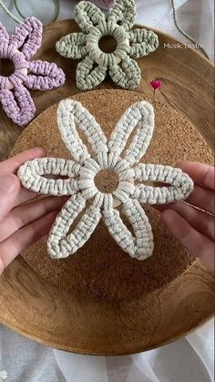 someone is holding up some crocheted flowers on a wooden platter with yarn