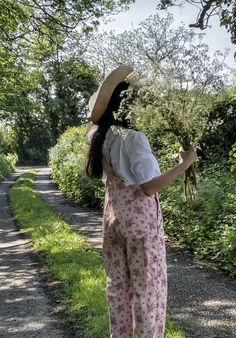 a woman with a straw hat on walking down a path in the grass and flowers