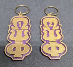 two gold and purple key chains with the letter p on them, sitting next to each other