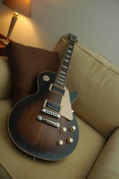 a black and white photo of an electric guitar on a couch with a lamp in the background