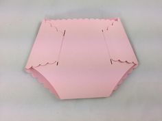 a piece of pink paper with scalloped edges on a white surface, cut out to look like an origami