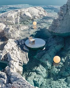 an outdoor table and chairs in the middle of a rocky area with blue water below