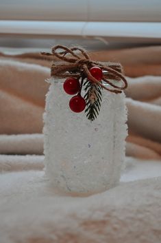 a glass jar filled with snow and berries on top of a bed covered in blankets