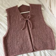 a pink sweater vest with a bow at the neck on a white bedding sheet