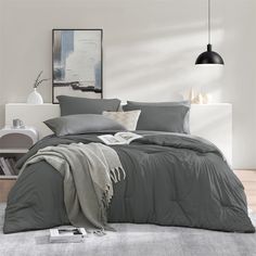 a bed with grey sheets and pillows in a room next to a white wall,