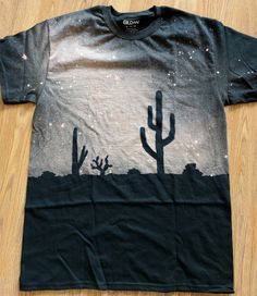 a black t - shirt with cactus and stars on it sitting on top of a wooden floor