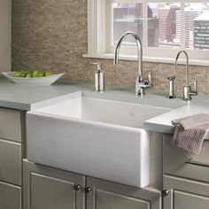 a kitchen sink sitting under a window next to a bowl of fruit on the counter