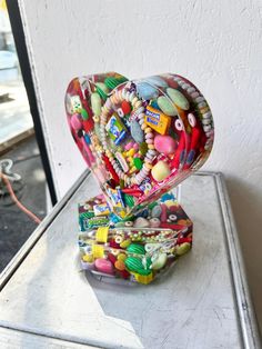 a heart shaped box filled with candy on top of a white table next to a window