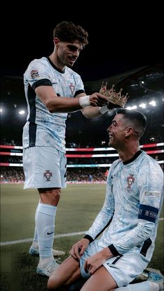 two soccer players are sitting on the field and one is holding a crown while the other holds his hand