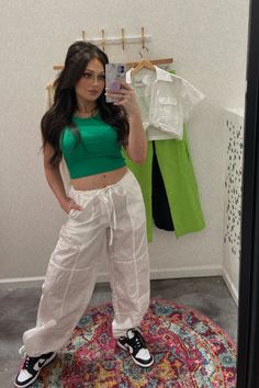 Mirror selfie featuring a fashion-forward outfit consisting of white cargo pants and a green tank top. The person is standing in front of a mirror, posing confidently while showcasing the trendy ensemble. The white cargo pants are loose-fitting with multiple pockets, paired with a green tank top that has a relaxed fit. The outfit exudes effortless chic, perfect for a casual day out or a springtime fashion statement. Stylish Mirror Selfie, Green Tank Top Outfit, White Parachute Pants, White Cargo Pants Outfit, Parachute Cargo Pants, Stylish Mirror, White Cargo Pants, Parachute Cargo, Beachy Chic