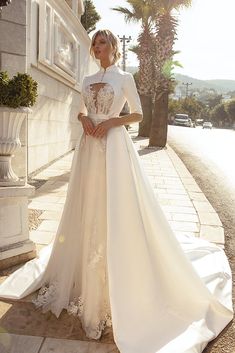 a woman in a white wedding dress standing on the side of a building with palm trees behind her